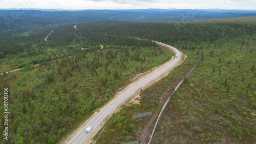 Scenic asphalt road with cars through the beautiful view of hills in Lapland during summer. Concept of roadtrip, travel, vacation, adventure.