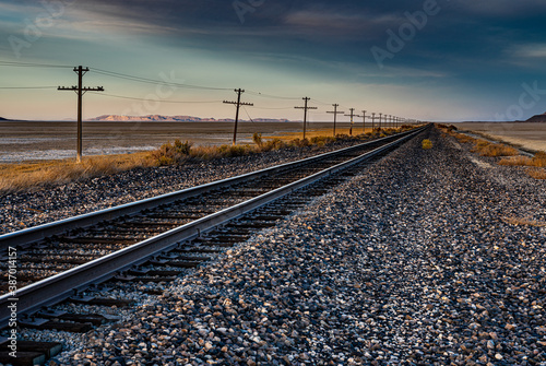 A nice landscape image of an old railroad track in the desert with a telegraph line next to it and mountains in the background. This beautiful image was taken during a gold hour sunset.