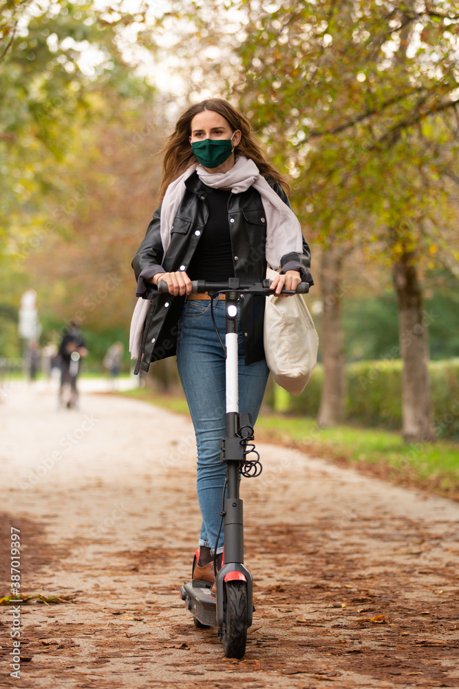 Casual caucasian teenager wearing protective face mask riding urban  electric scooter in city park during covid pandemic. Urban mobility  concept. foto de Stock | Adobe Stock