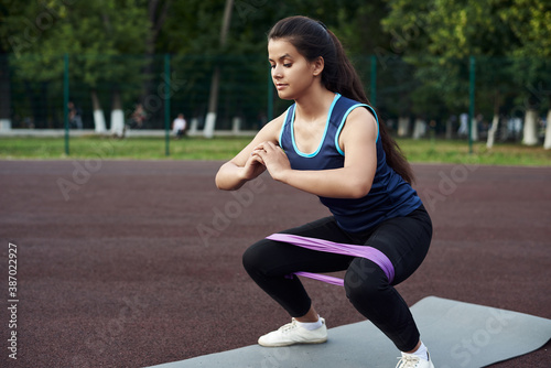 Young woman goes in for sports using an elastic band for fitness. A beautiful sportive girl shakes her legs with an expander