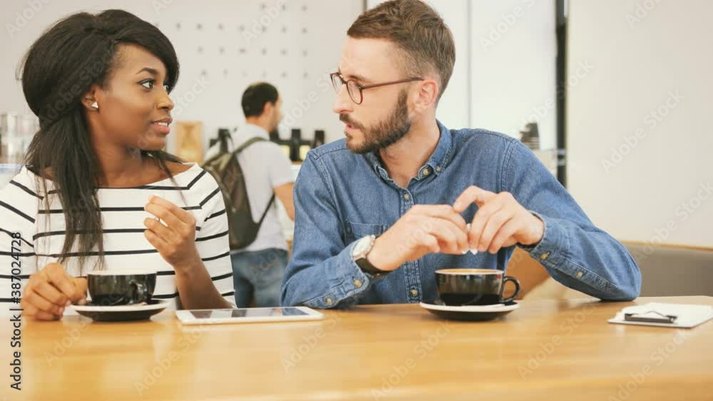 Close up portrait of handsome caucasian man and beautiful african american woman. Two sitting in cafe talking and pouring sugar into cups of coffee. Close up portrait of handsome caucasian man and beautiful african american woman. Two sitting in cafe talking and pouring sugar into cups of coffee.