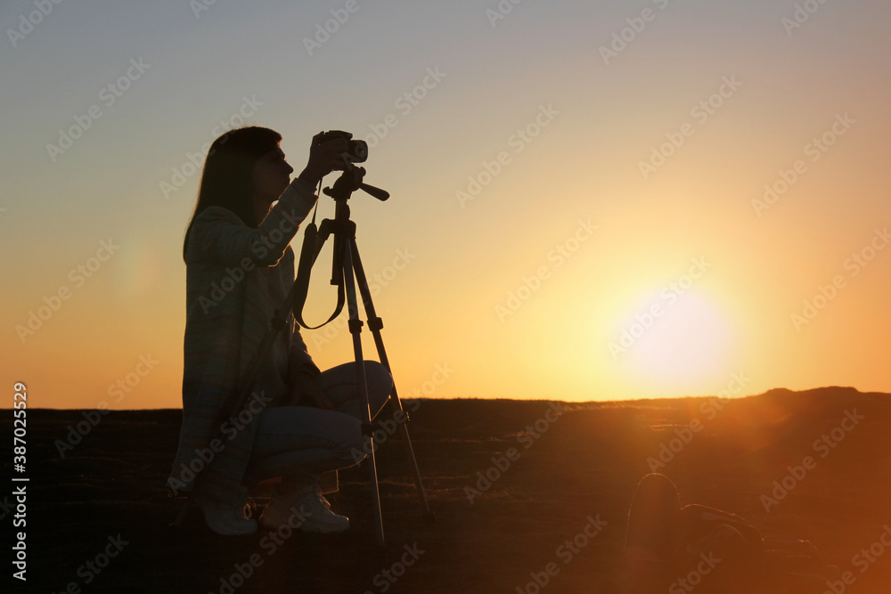 Silhouette of a woman photographer and camera on tripod against the background of the rising sun over the horizon. Photographer life concept.