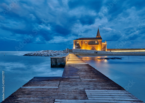 The church of Madonna of the Angel in Caorle, seen from the pier of the east beach at a dark and cloudy sunset at the end of summer (Santuario Madonna dell' Angelo) photo