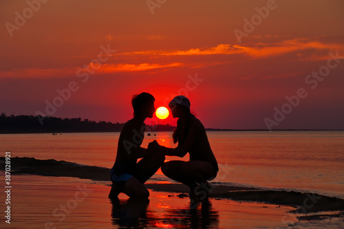 A couple in love is sitting on the beach at sunset