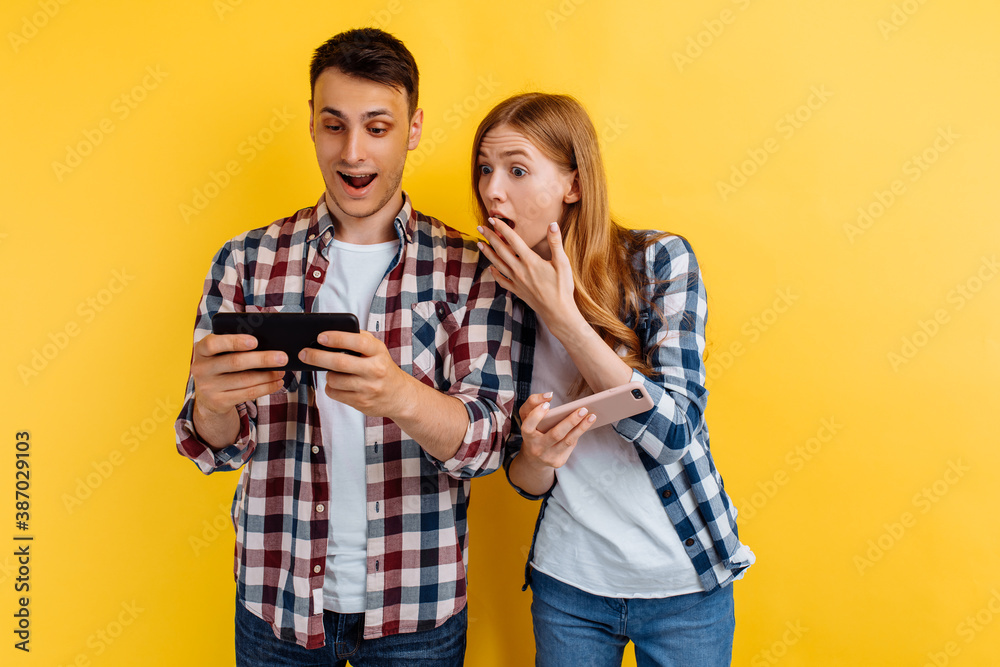 shocked couple, a man and a woman, play video games on a smartphone, yellow background shocked couple, a man and a woman, play video games on a smartphone, yellow background