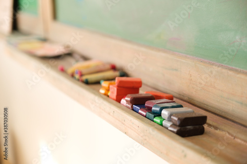 rectangle beeswax crayons lined up along shelf below chalkboard