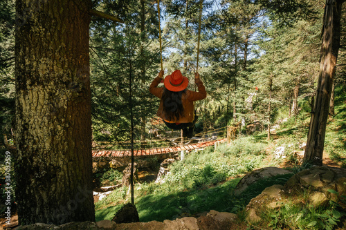Girl with orange hat swinging on a forest tree among the mountains photo
