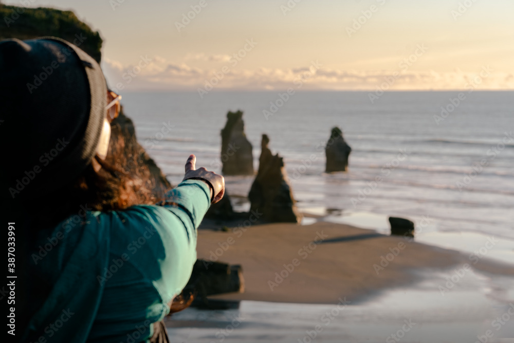 Woman pointing with her finger at big rock formations by the beach. Selective focus