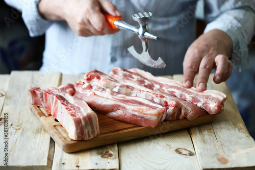 The chef cuts raw pork ribs on a wooden board. Selective focus. Cooking the ribs.