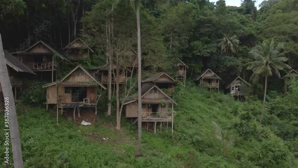 Ascending up drone, aerial birds eye view of old style wooden Thai bungalow resort that is now derelict and unused due to the effects of the covid pandemic on travel and tourism in South east Asia Ascending up drone, aerial birds eye view of old style wooden Thai bungalow resort that is now derelict and unused due to the effects of the covid pandemic on travel and tourism in South east Asia