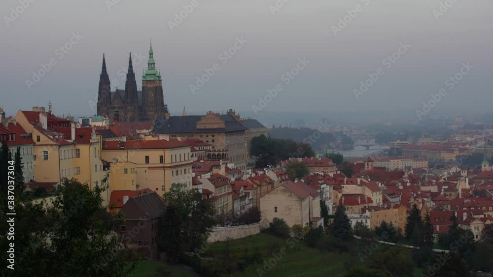 Prague skyline during sunrise in spring. Towers of St Vitus and St. Nicholas church seen from Petrin hill viewpoint. Romantic golden sun glow in morning and blooming trees in a park Prague skyline during sunrise in spring. Towers of St Vitus and St. Nicholas church seen from Petrin hill viewpoint. Romantic golden sun glow in morning and blooming trees in a park