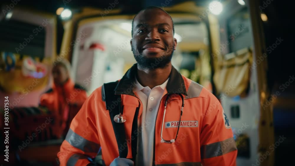 Portrait of a Black African American EMS Paramedic Proudly Standing in Front of Camera in High Visibility Medical Orange Uniform and Smiling. Successful Emergency Medical Technician or Doctor at Work.