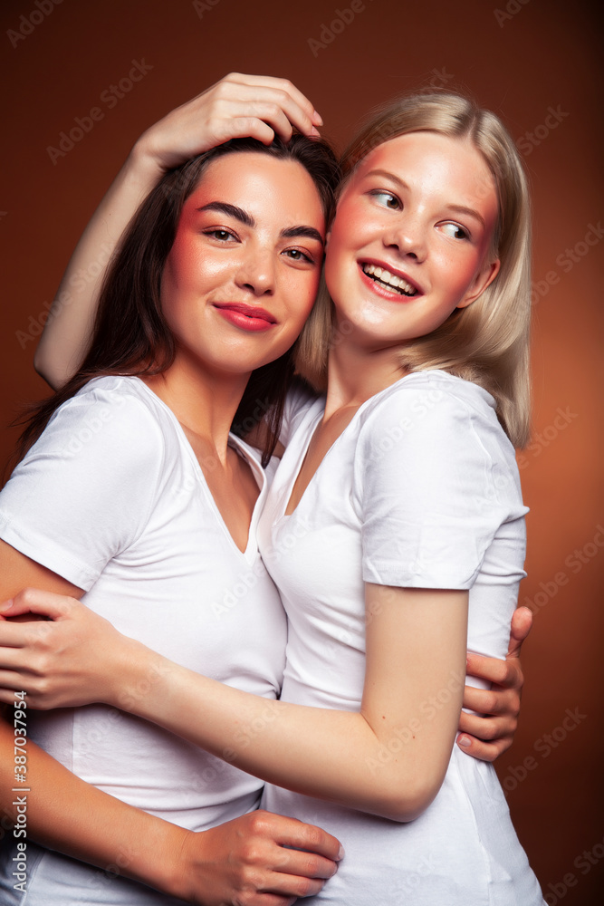 wo pretty diverse girls happy posing together: blond and brunette on brown background, lifestyle people concept wo pretty diverse girls happy posing together: blond and brunette on brown background, lifestyle people concept