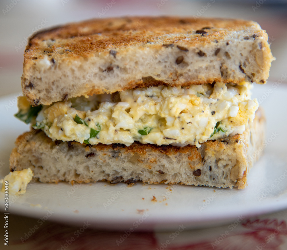 Half Egg Salad Sandwich made from Toasted Sourdough Whole Grain Bread on White Plate Half Egg Salad Sandwich made from Toasted Sourdough Whole Grain Bread on White Plate