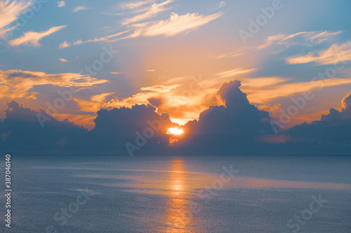 Sun rising from the sea. Colorful cloudy blue sky and sunbeams