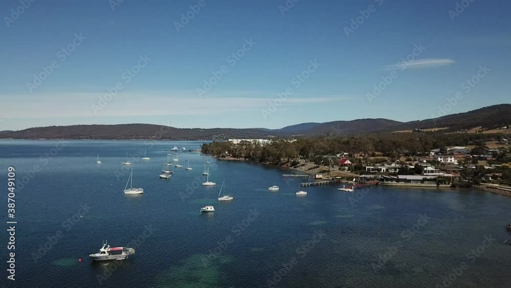 Aerial drone pan around collection of boat and yachts in deep blue sea surrounded by small mountain range and town on clear sunny day Aerial drone pan around collection of boat and yachts in deep blue sea surrounded by small mountain range and town on clear sunny day