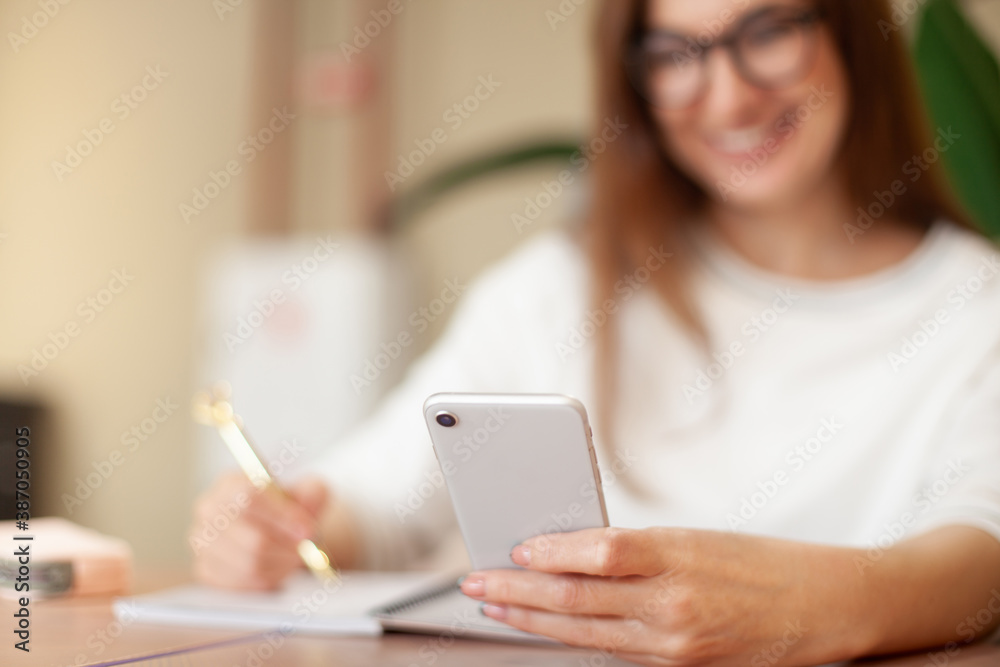 Concentrated young woman writing to do list in notepad and using task management mobile application Concentrated young woman writing to do list in notepad and using task management mobile application
