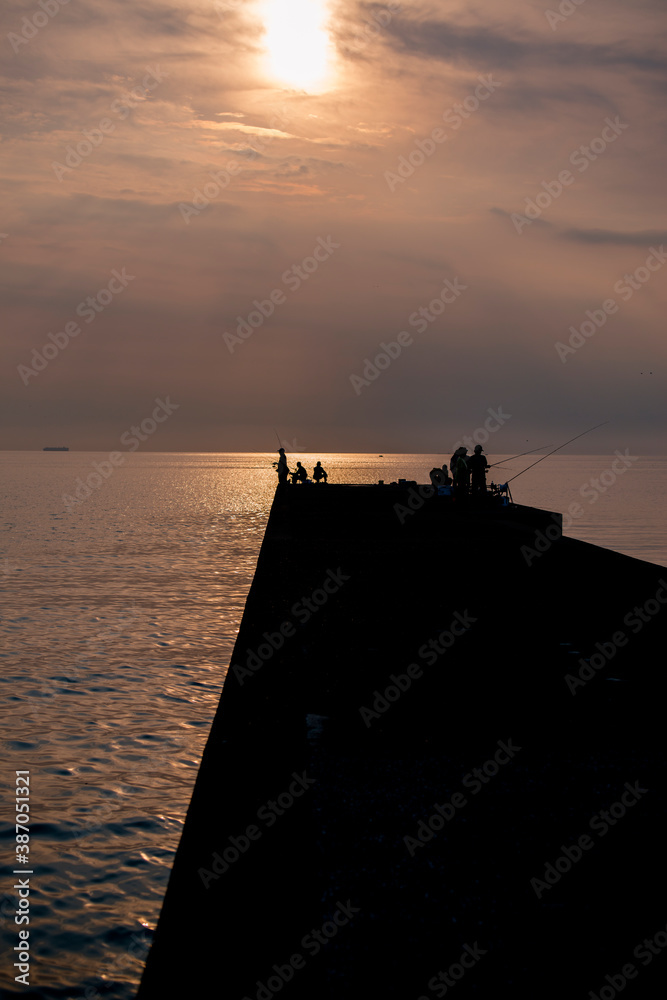 夕日に照らされた堤防で釣りを楽しむ人々 夕日に照らされた堤防で釣りを楽しむ人々