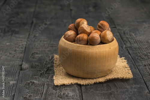 A tall wooden bowl with large hazelnuts on a black wooden table.