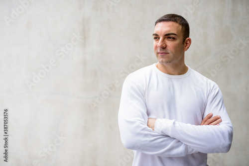 Handsome man thinking with arms crossed against concrete wall