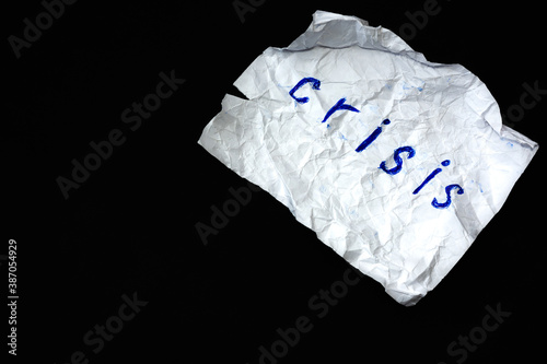 White crumpled sheet of paper with the words "Crisis" on a black background. Copy space. Top view. Global world economy collapse concept