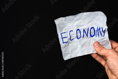 Holding white crumpled piece of paper in hand with inscription "Economy". Global world economy collapse concept. Copy space