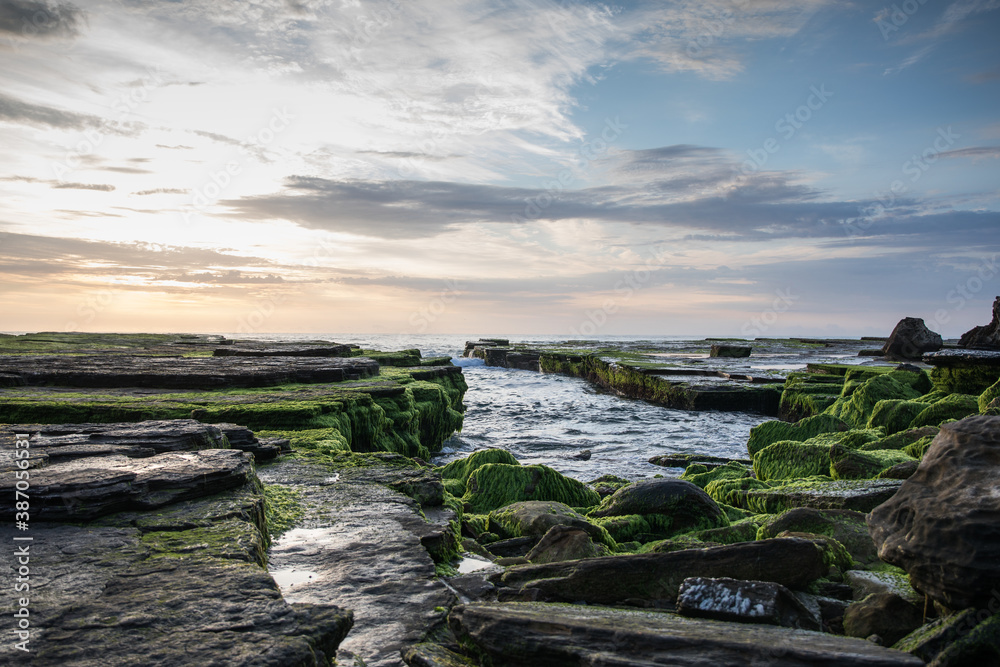 Rocks covered with green moss on the coastline with lapping waves at sunrise