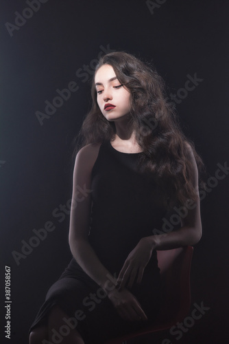 Vintage portrait with harsh light of a beautiful, slim brunette woman with bright makeup and wavy hair