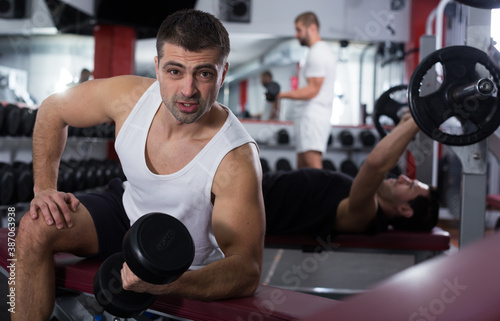 Muscular young man doing exercises with dumbbells at gym