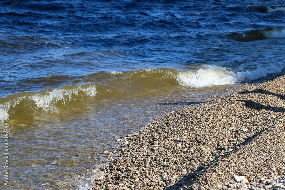 waves run onto the shore and crash against the rocks, creating many splashes and splashes near the shore. river surf in stormy weather near a stone pebble coast with foamy splashing waves. waves run onto the shore and crash against the rocks, creating many splashes and splashes near the shore. river surf in stormy weather near a stone pebble coast with foamy splashing waves.