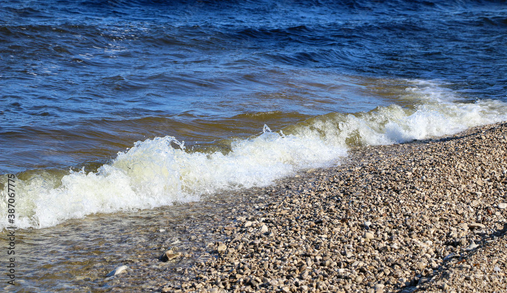 waves run onto the shore and crash against the rocks, creating many splashes and splashes near the shore. river surf in stormy weather near a stone pebble coast with foamy splashing waves. waves run onto the shore and crash against the rocks, creating many splashes and splashes near the shore. river surf in stormy weather near a stone pebble coast with foamy splashing waves.