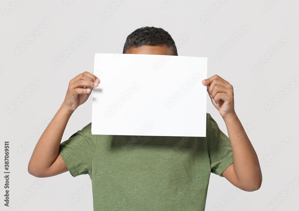 Little African-American boy with blank paper sheet on light background Little African-American boy with blank paper sheet on light background