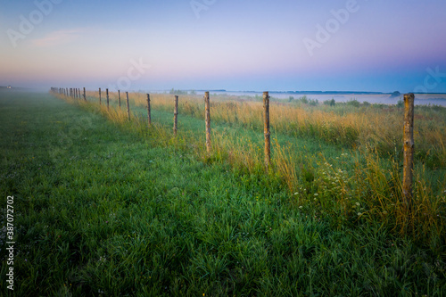 Morning fog in the meadows during sunrise in the countryside. Rural landscape with a fog on the geen field. the fence stretching into the distance.