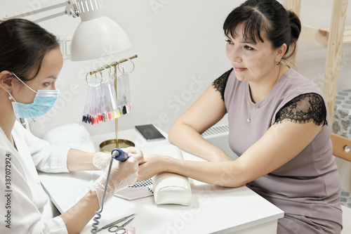 Gorgeous mid age woman getting her nails done by a manicurist in a beauty salon. hardware manicure. real people. side view. beauty salon as a small business.