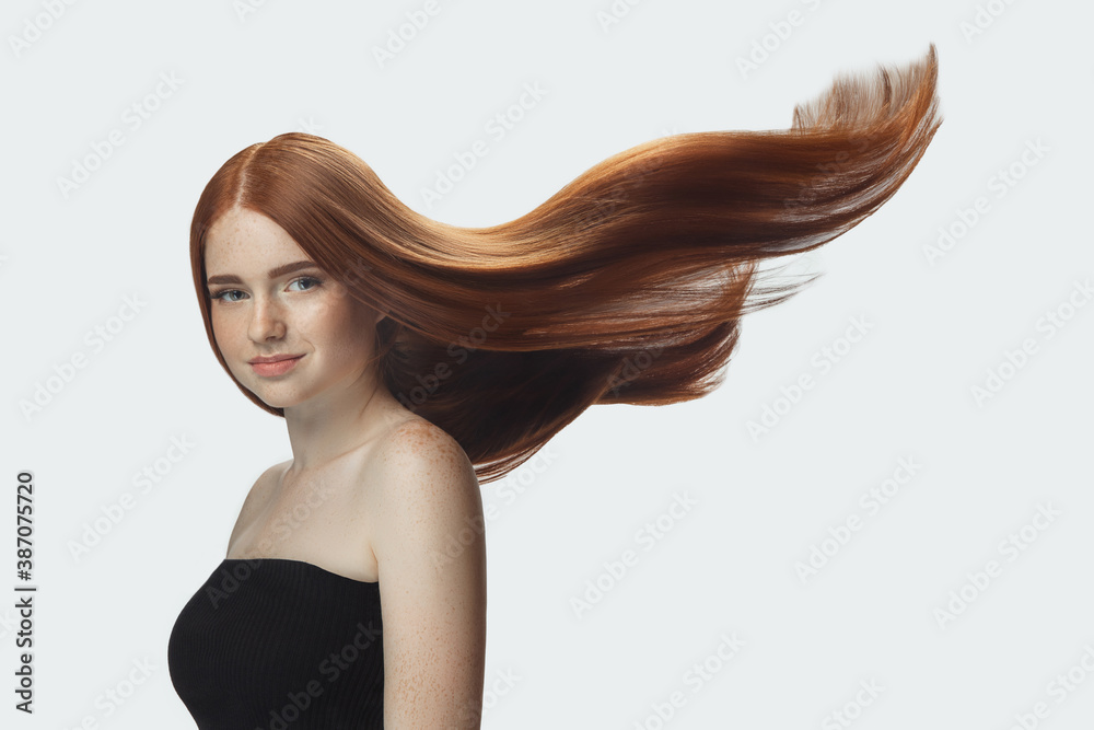 Beautiful model with long smooth, flying red hair isolated on white studio  background. Young caucasian girl with well-kept skin and hair blowing on air.  Concept of salon care, beauty, fashion. Stock Photo |
