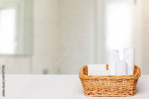 Basket with bath accessories such as soap bars, Cream and cosmetic tissues for body care on a white table over blurred bath background with copy space. For your product display montage.