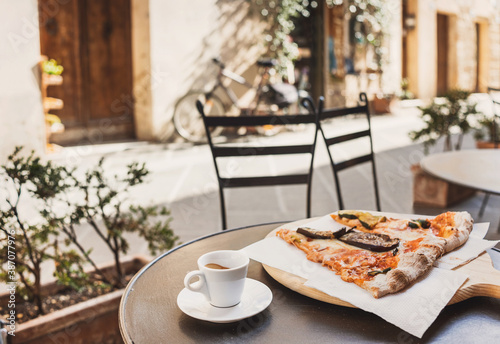 Fototapeta Naklejka Na Ścianę i Meble -  Vacations in Italy. Cup of espresso coffee with slices of pizza with beautiful italian street on the background.