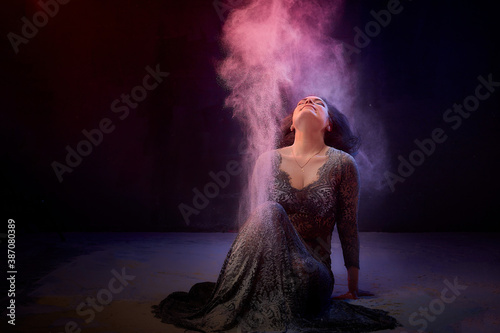 Girl in black dress posing in dark studo during photoshoot with flour or dust and light. Dangerous witch during struggle between good and evil photo