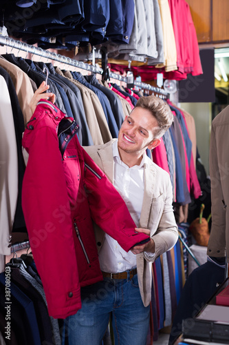 Young male customer examining coats in men cloths store