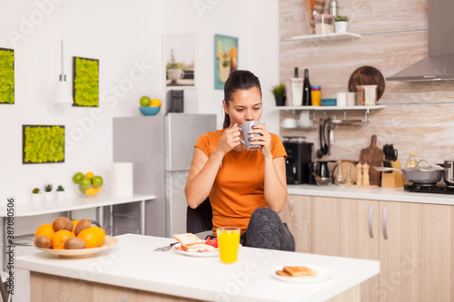 Taking a sip of coffee in the morning while enjoying delicious breakfast. Lady ejoying a cup of coffee in the morning. Happy housewife relaxing and spoiling herself with a healthy meal alone
