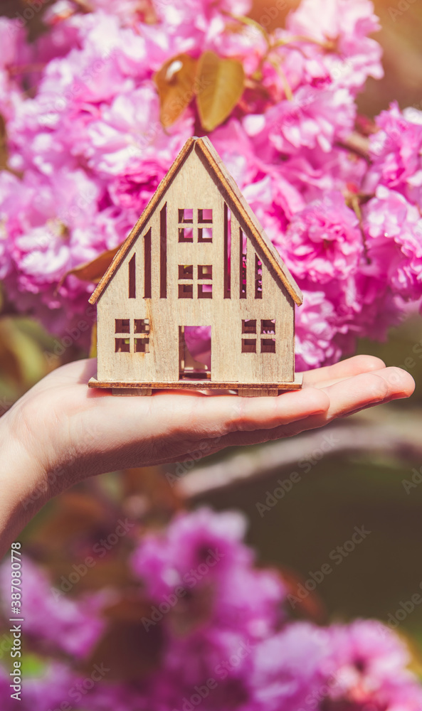 The girl holds the house symbol against the background of blossoming Sakura

