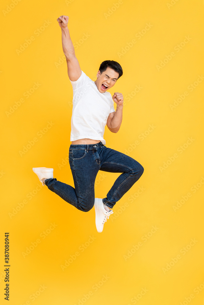 Young energetic Asian man  jumping and raising his fist isolated on yellow color background - obrazy, fototapety, plakaty 