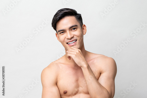 Shirtless handsome Asian man posing with hand touching chin on isolated gray background