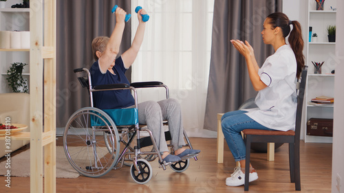 Old lady in wheelchair exercising with dumbbelss. Nurse helping with rehabilitation. Training  sport  recovery and lifting  old person retirement home  healthcare nursing  health support  social