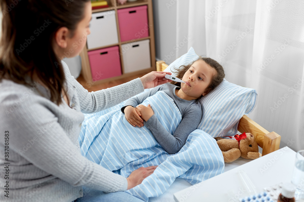 family, health and people concept - mother and sick little daughter lying in bed with oral thermometer and measuring temperature at home family, health and people concept - mother and sick little daughter lying in bed with oral thermometer and measuring temperature at home