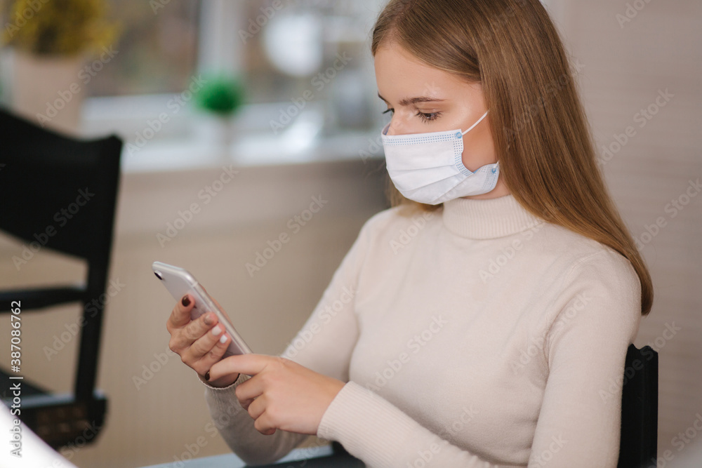 Female customer in beauty salon sitting in medical mask and use phone. Beautiful young blond hair woman wiating for brow master Female customer in beauty salon sitting in medical mask and use phone. Beautiful young blond hair woman wiating for brow master