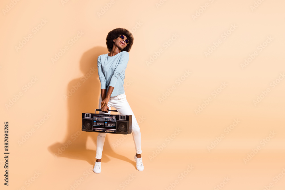 Photo portrait of attractive african american girl holding boom-box in two hands laughing isolated on pastel beige colored background