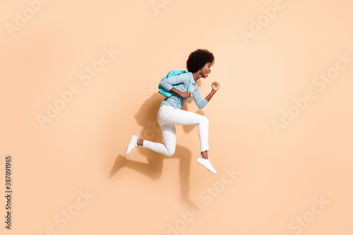 Photo portrait of black skinned woman hurrying running jumping up with blue rucksack isolated on pastel beige colored background