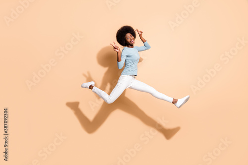 Photo portrait of african american girl holding two v-signs flying in air isolated on pastel beige colored background