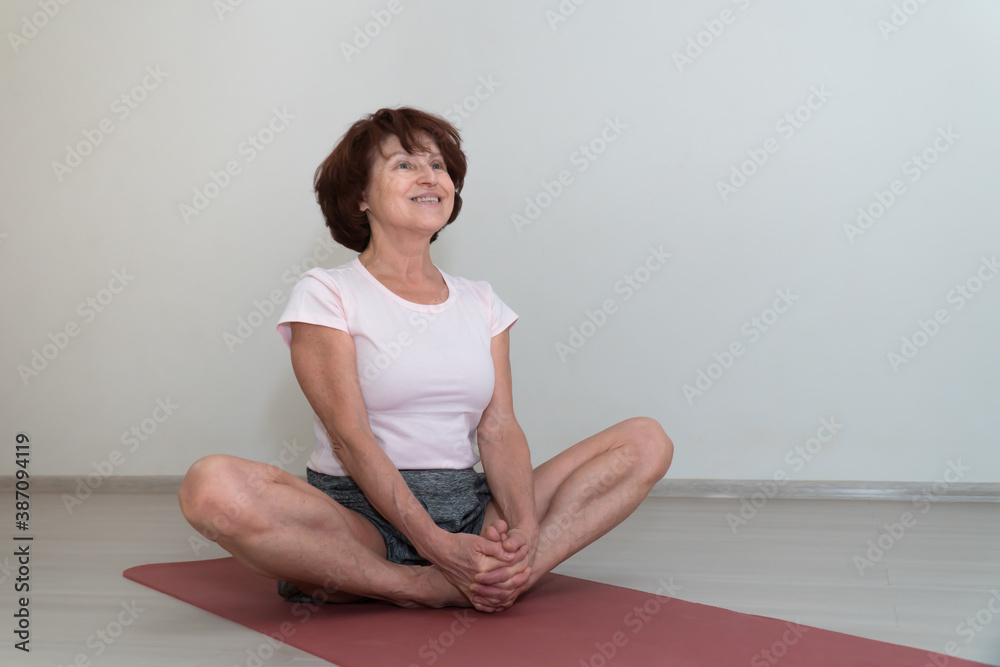 Senior caucasian lady with short hair do yoga asana batterfly pose indoor